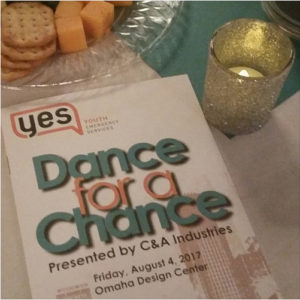 The event program for YES Dance with a Chance, on a table with a votive candle and a plate of cheese and crackers.